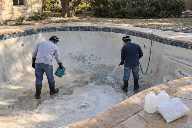 Workers in face shields and chemical gloves acid washing a drained pool