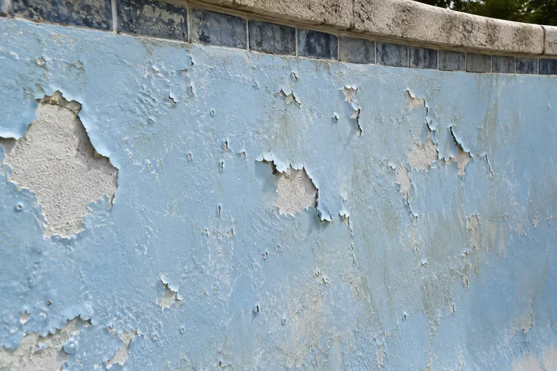 Old pool paint blistering and peeling off a plaster wall