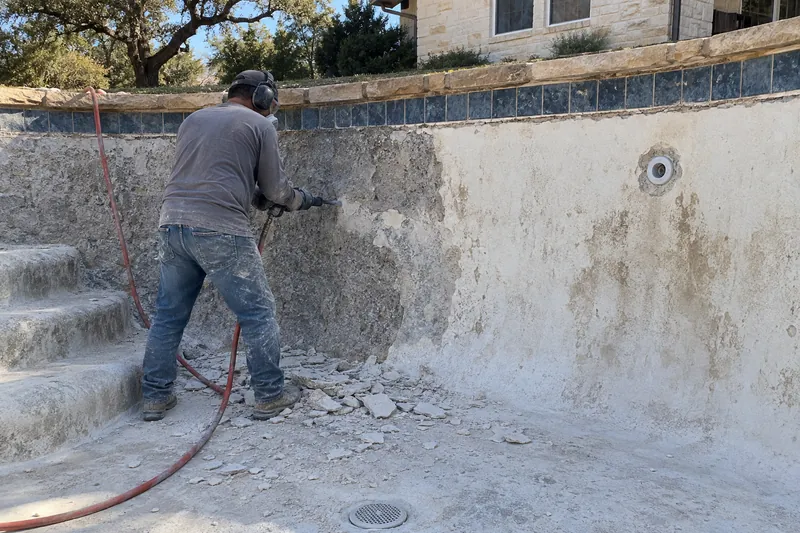 Old plaster being chipped off to bare gunite below the waterline tile