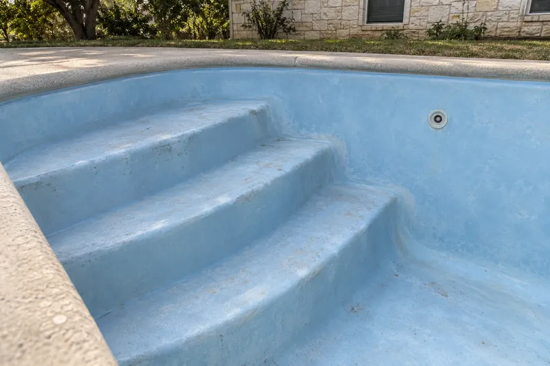 Faded, chalky gelcoat on the steps of a drained fiberglass pool