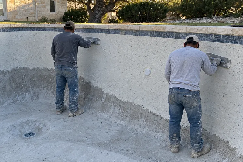 Finishers troweling fresh quartz plaster onto a pool wall